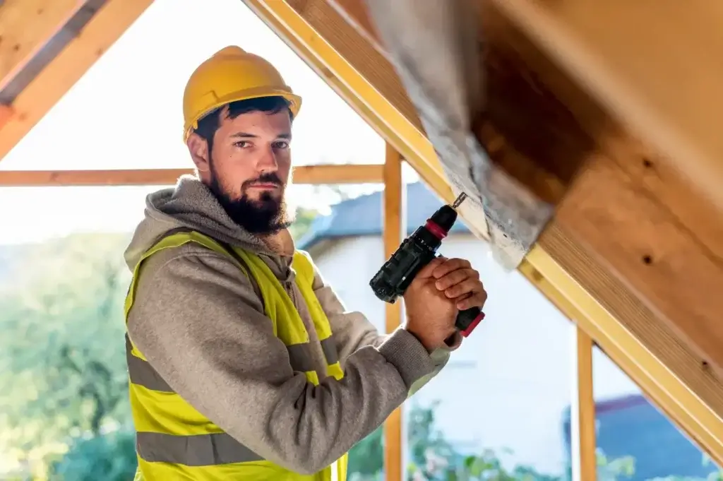 Man in hard hat and safety vest holding a drill, ready for metal roof repair.